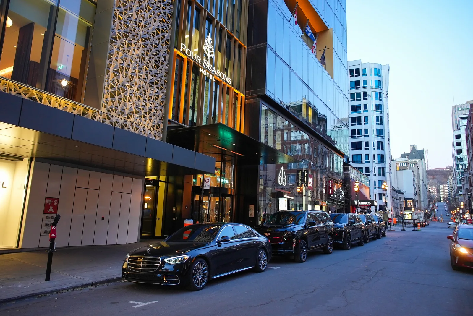 Mercedes sedan and Cadillac SUVs outside Four Seasons Hotel Montréal.